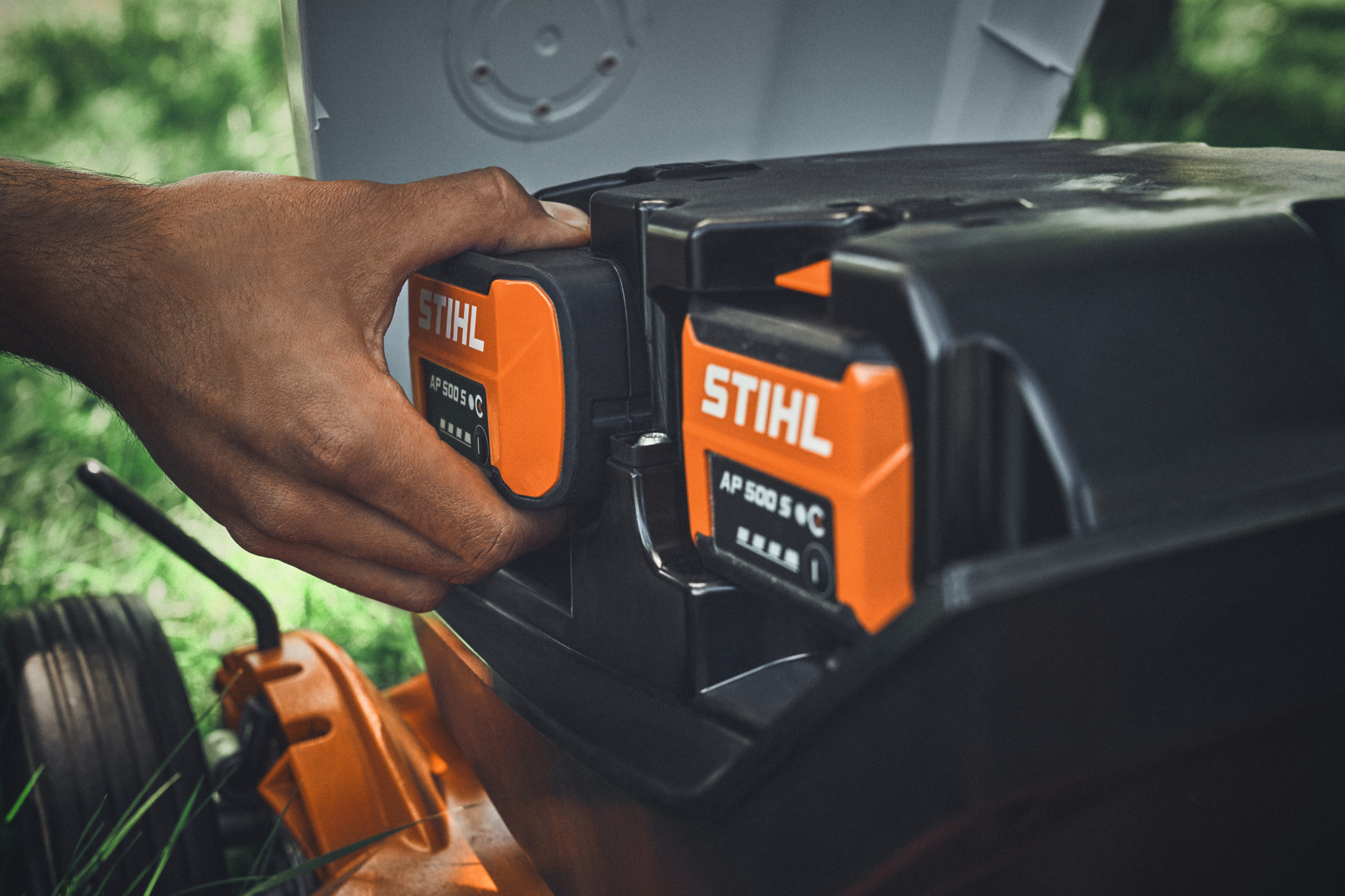 Une personne insère une batterie STIHL AP 500 S dans une tondeuse à batterie STIHL