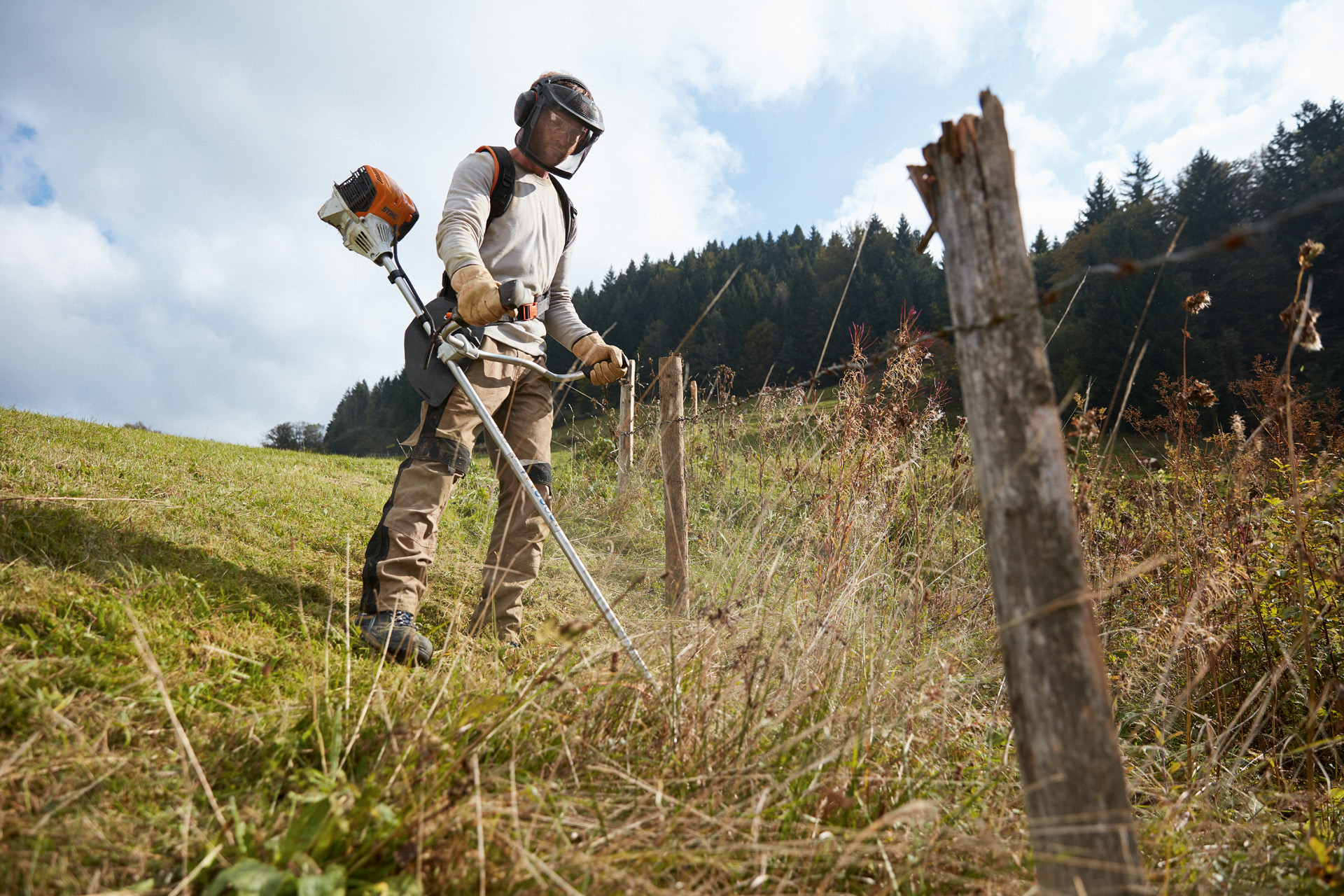 Un homme en équipement de protection tond le gazon avec un coupe-bordures à essence STIHL FS 91