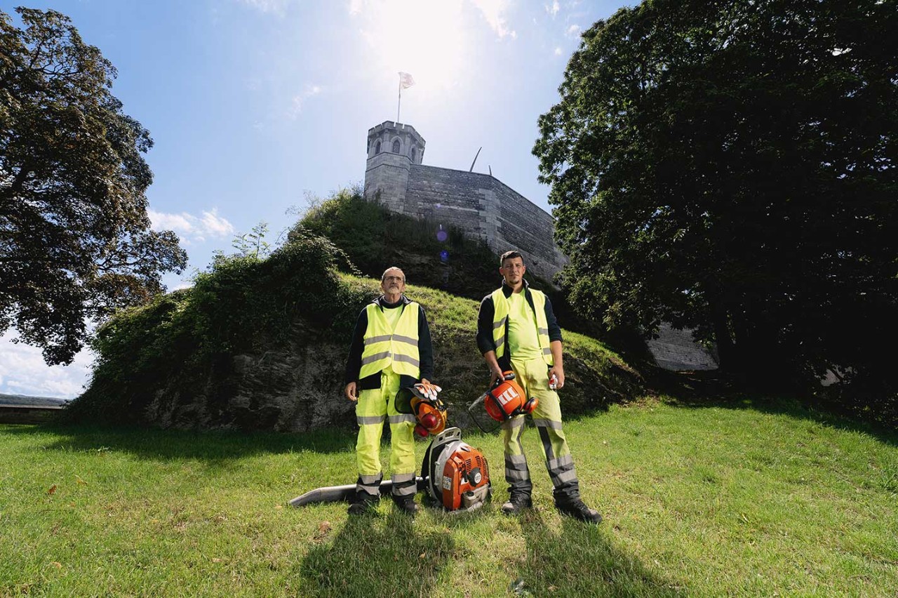 Bernard et Jérémy posent avec un  souffleur de feuilles et des équipements de sécurité dans la verdure autour de la Citadelle de Namur.