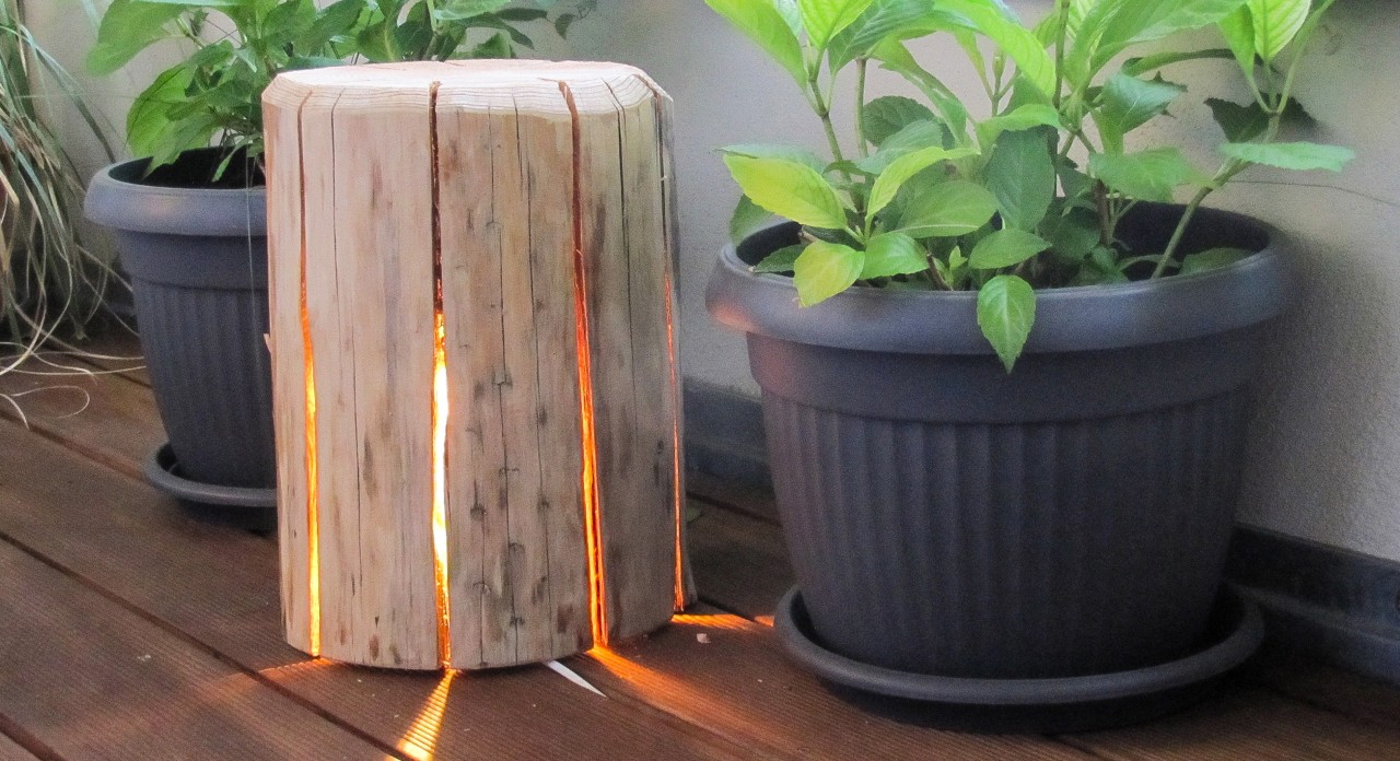Lampe en bois à construire soi-même entre deux pots de fleurs, une guirlande lumineuse illumine l’intérieur