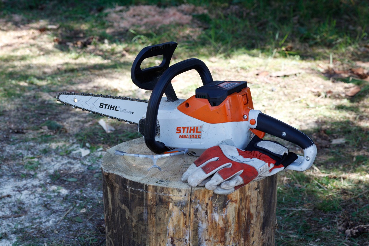 Une tronçonneuse à batterie STIHL MSA 140 C et des gants de protection sur une souche d’arbre