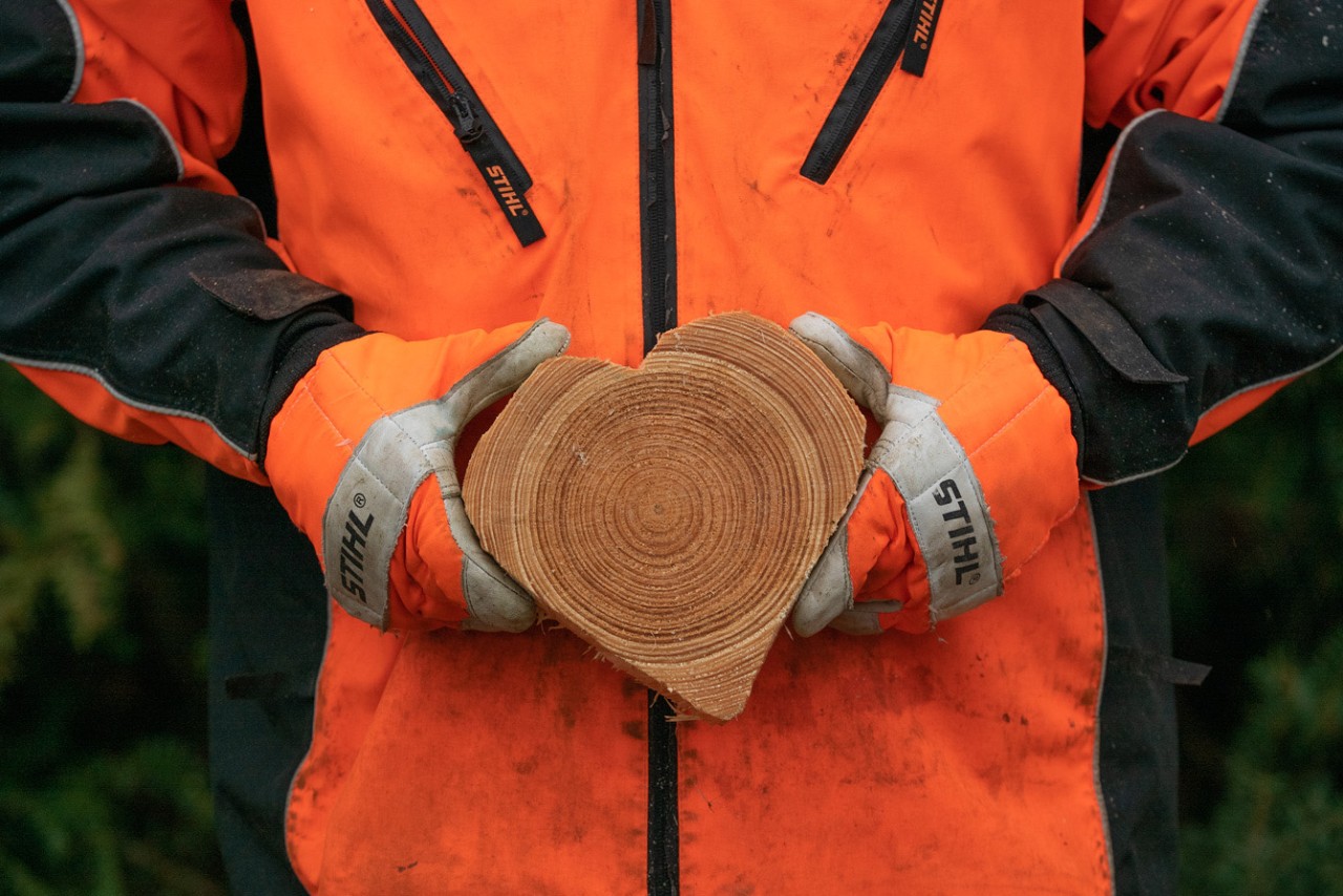 Cœur en bois sculpté dans les mains d’une personne portant des vêtements de protection STIHL