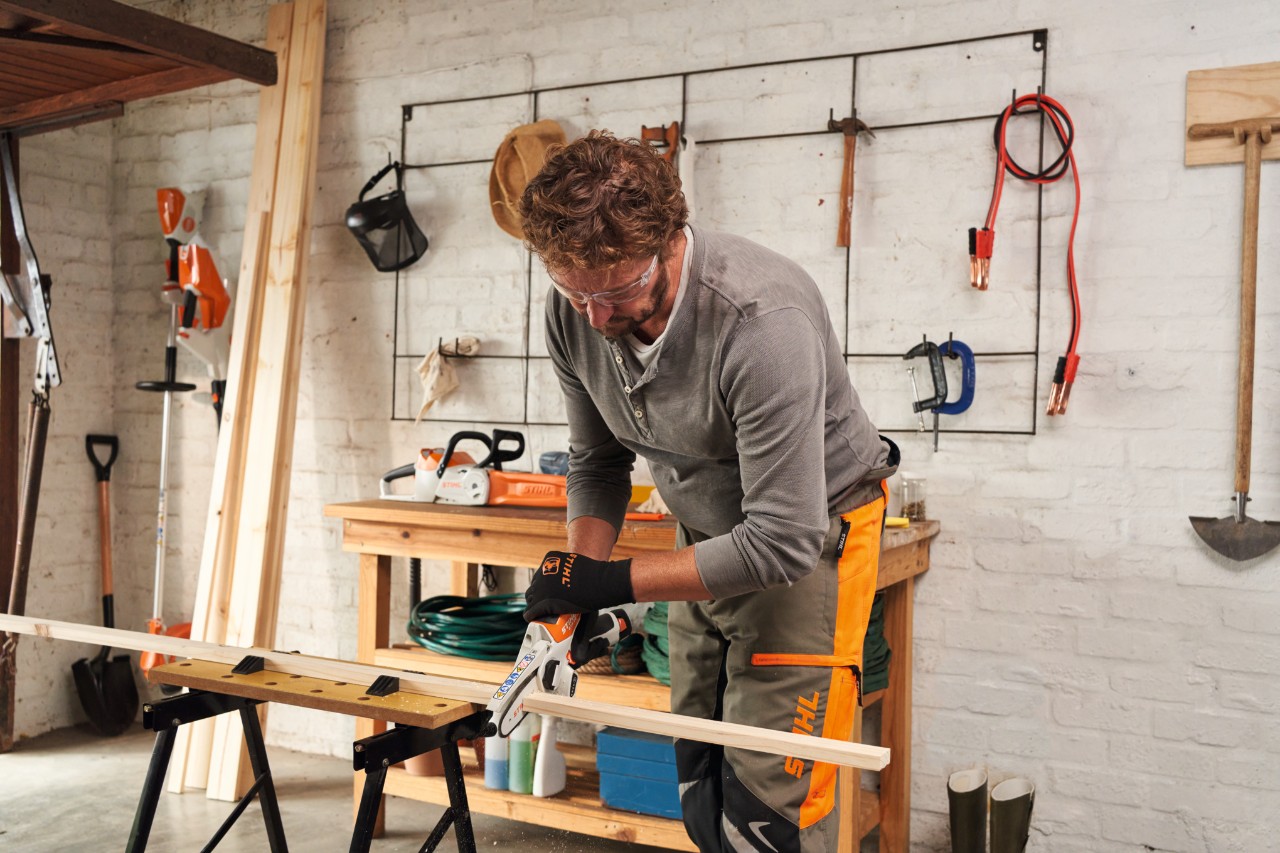 Dans un atelier, un homme coupe de fines planches de bois avec la scie de jardin à batterie STIHL GTA 26