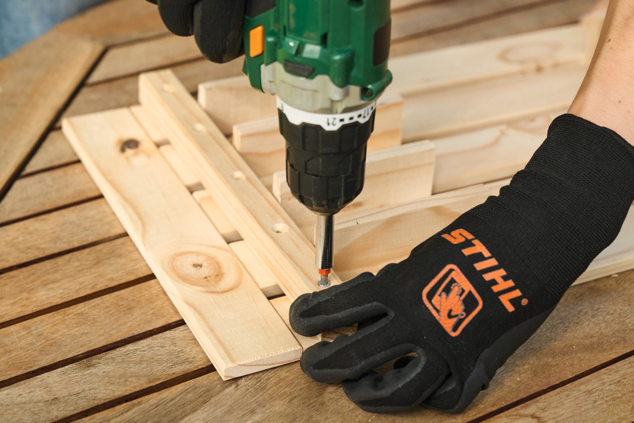 Gros plan sur une personne portant des gants de protection STIHL réalisant le perçage préalable des trous