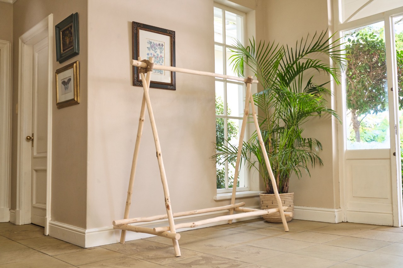 Portant à vêtements en bois de fabrication « maison » dans une pièce, en arrière-plan une plante en pot et un cadre photo