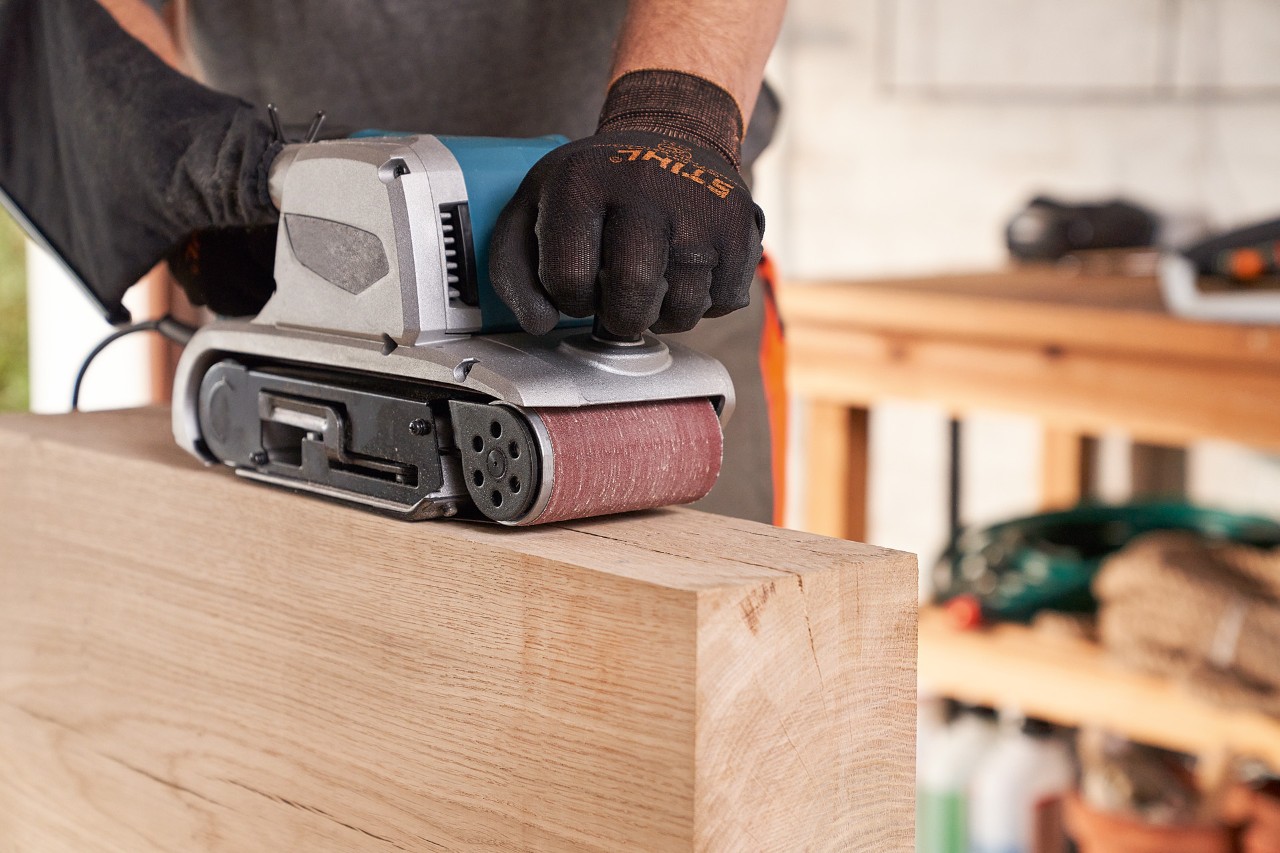 Gros plan sur une personne portant des gants de protection STIHL lors du ponçage du bois avec une meuleuse en atelier
