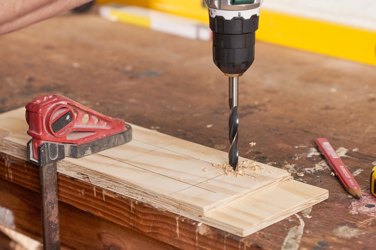 Utilisez une visseuse sans fil pour percer un trou dans une fine planche de bois afin de réaliser un gabarit de perçage