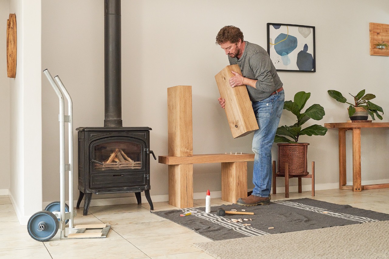 Un homme à l’intérieur assemble des poutres en bois pour fabriquer un meuble de rangement de bois de chauffage 