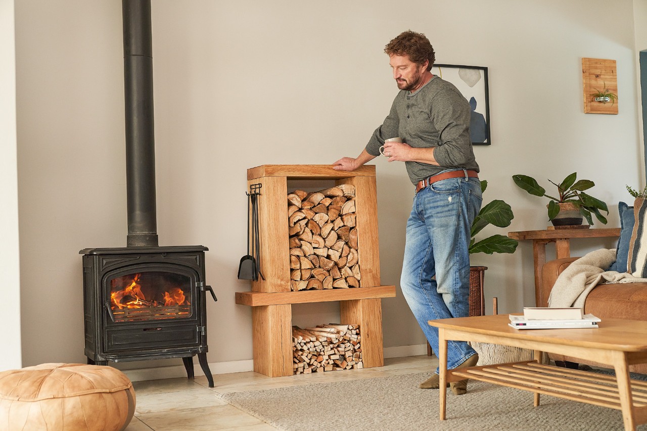 Homme debout dans un intérieur meublé, devant un meuble de rangement de bois fabriqué soi-même, une tasse à la main