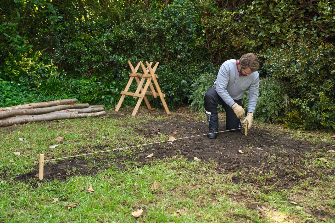 Homme plantant des piquets dans le sol reliés par une ficelle pour délimiter la surface