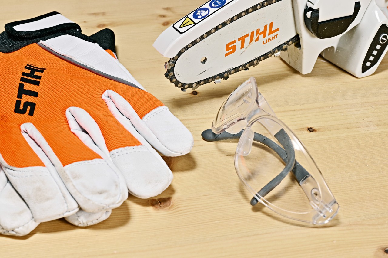 Scie de jardin sur batterie STIHL GTA 26, gants de sécurité STIHL et  lunettes de protection sur un établi en bois