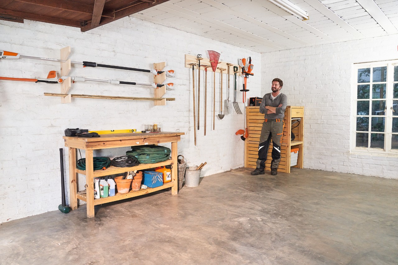Homme dans un atelier avec un support d'outils de jardinage qu'il a lui-même fabriqué et divers outils STIHL, dont des débroussailleuses et des casse-feuilles.