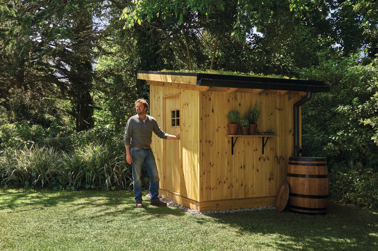 Homme en jeans sur un terrain de jardin devant une cabane à outils qu'il a lui-même construite