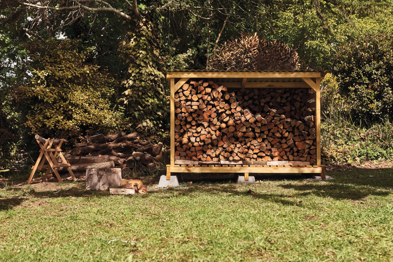 Abri à bois artisanal sur un terrain de jardin, rempli de bûches de bois   