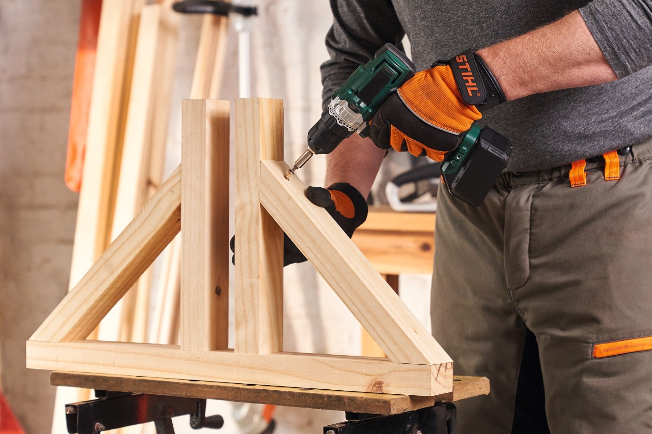 Une personne portant des gants de protection STIHL Function Protect en train de visser les pieds pour construire un brise-vue
