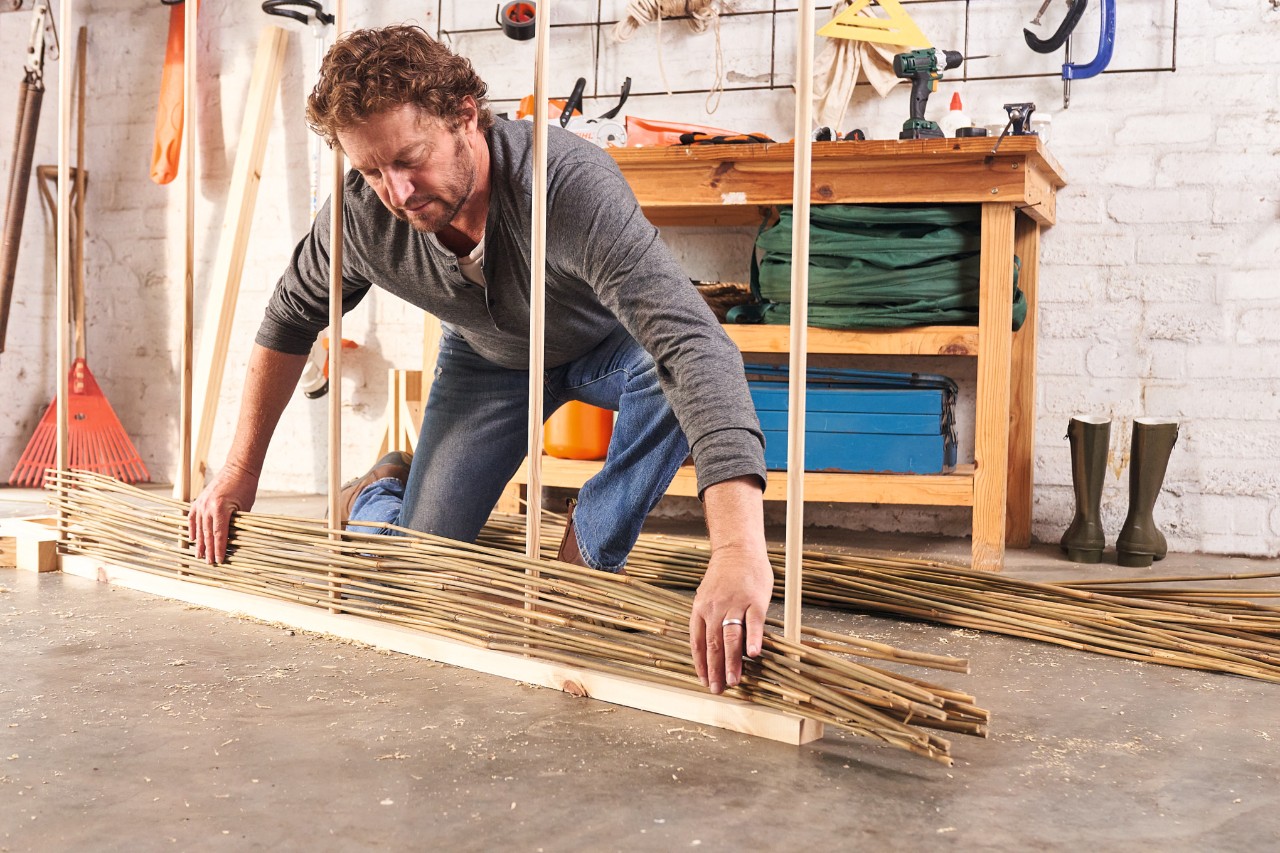 Un homme en train de tresser les tiges de bambou pour construire un brise-vue