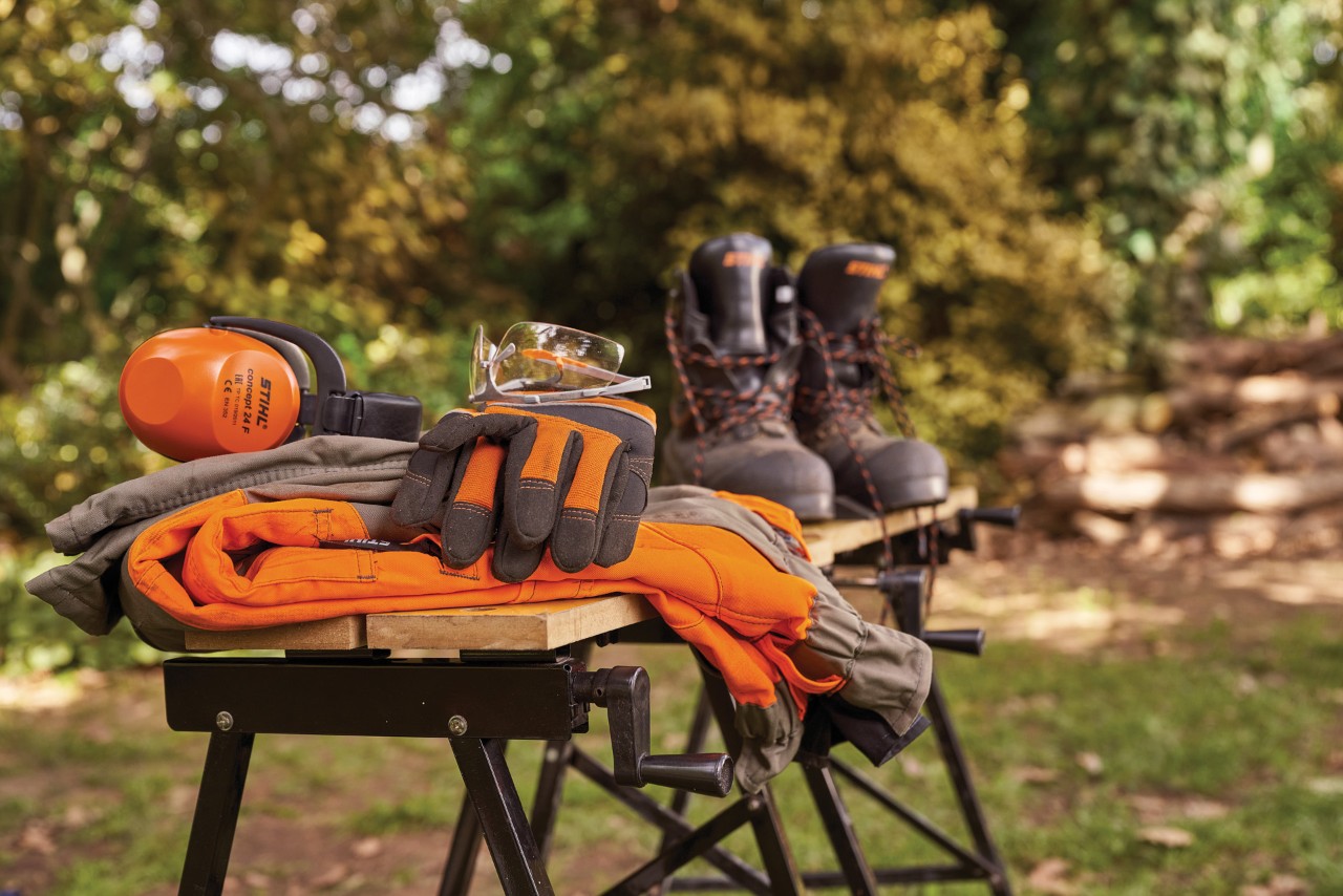 Protection auditive STIHL, bottes, lunettes et gants de protection sur un établi dans un jardin