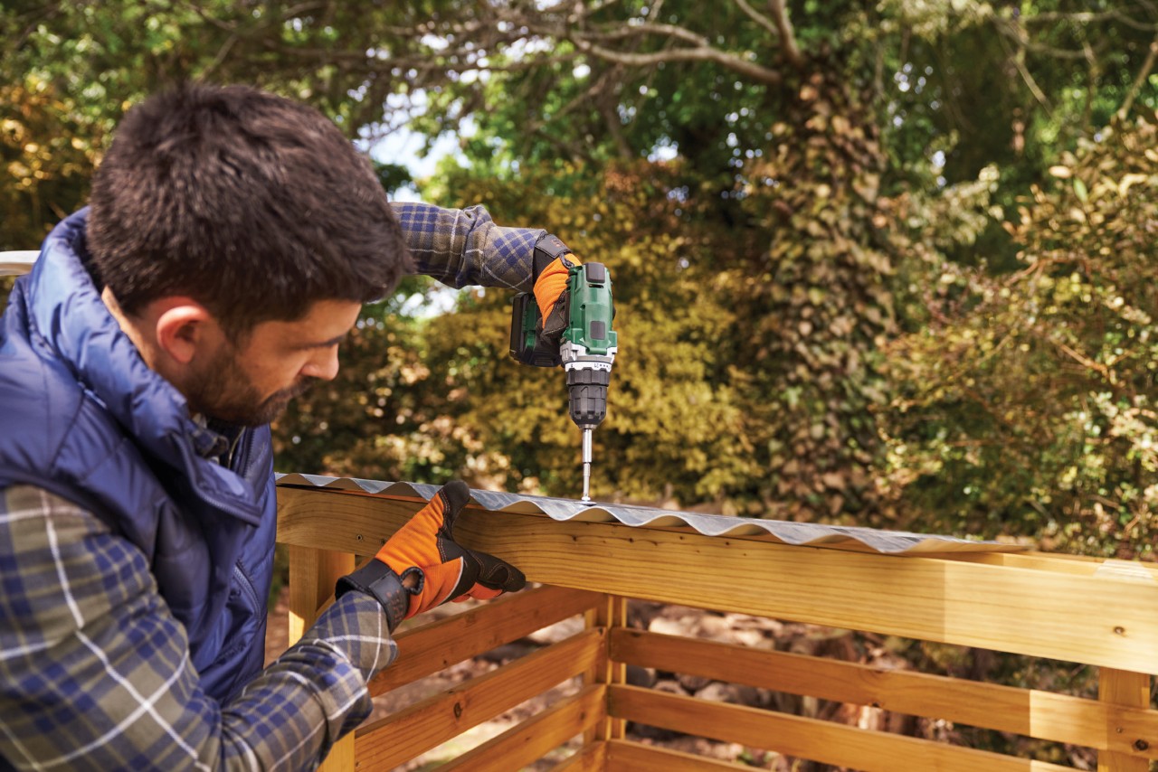Comment fabriquer un range-bûches : homme fixant une tôle ondulée sur un range-bûches en bois