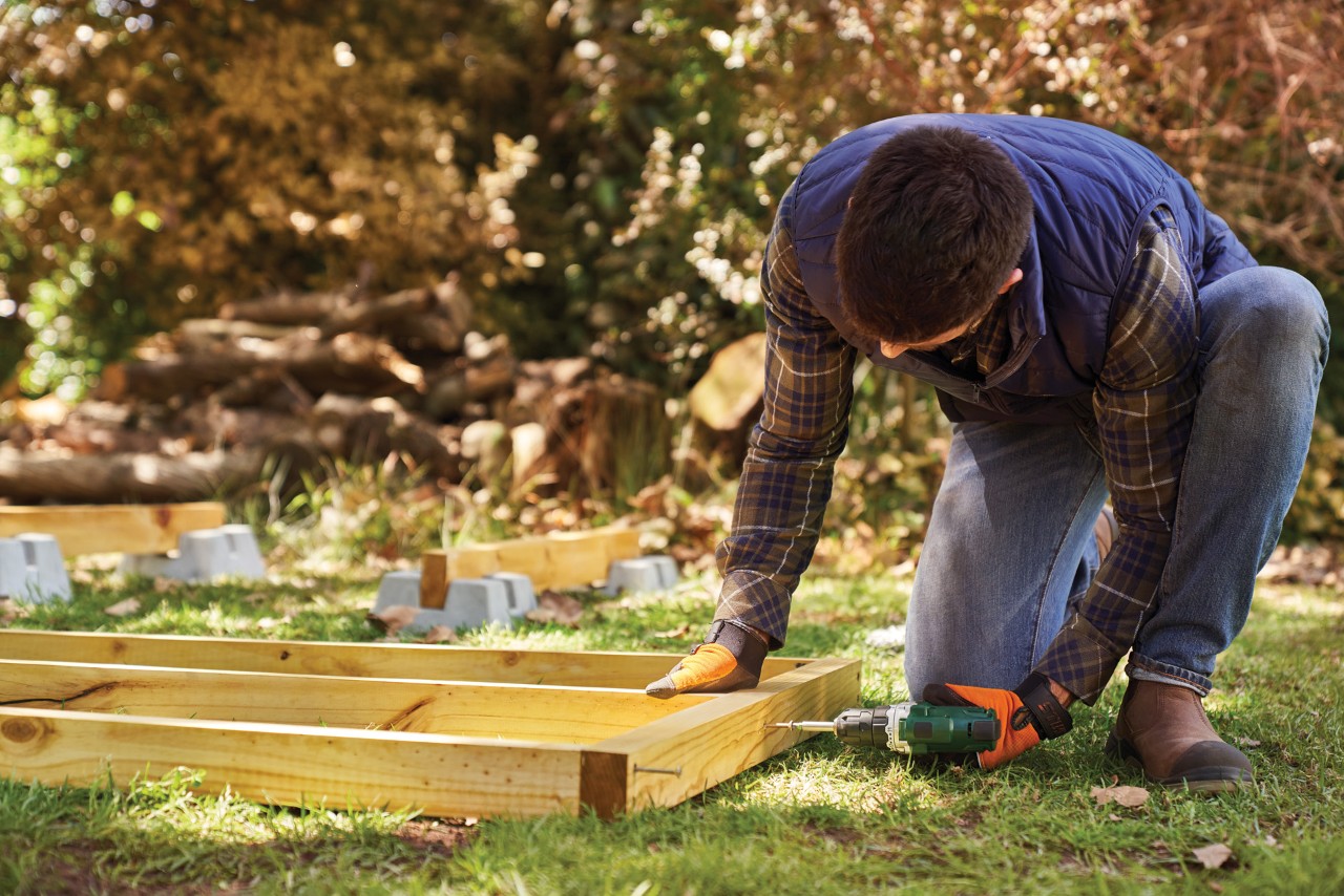 Comment fabriquer un range-bûches : un homme visse la charpente de plancher