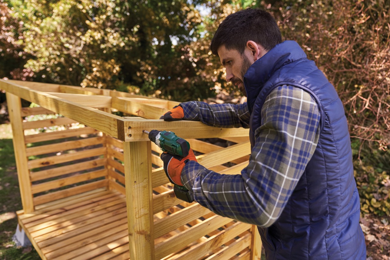 Comment fabriquer un range-bûches : homme vissant le cadre en bois de l’abri à bûches