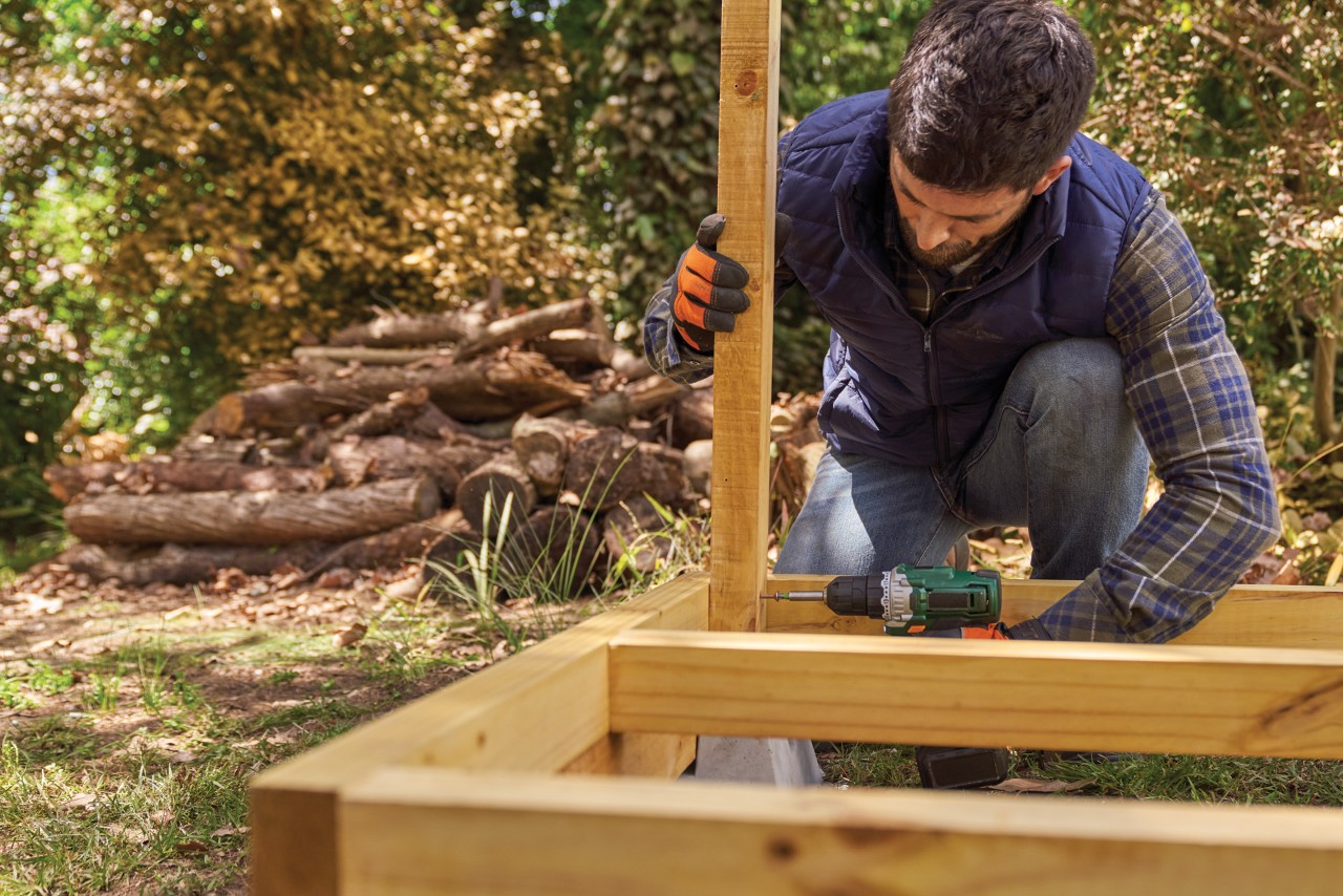 Comment fabriquer un range-bûches : homme fixant un montant sur une charpente de plancher déjà construite