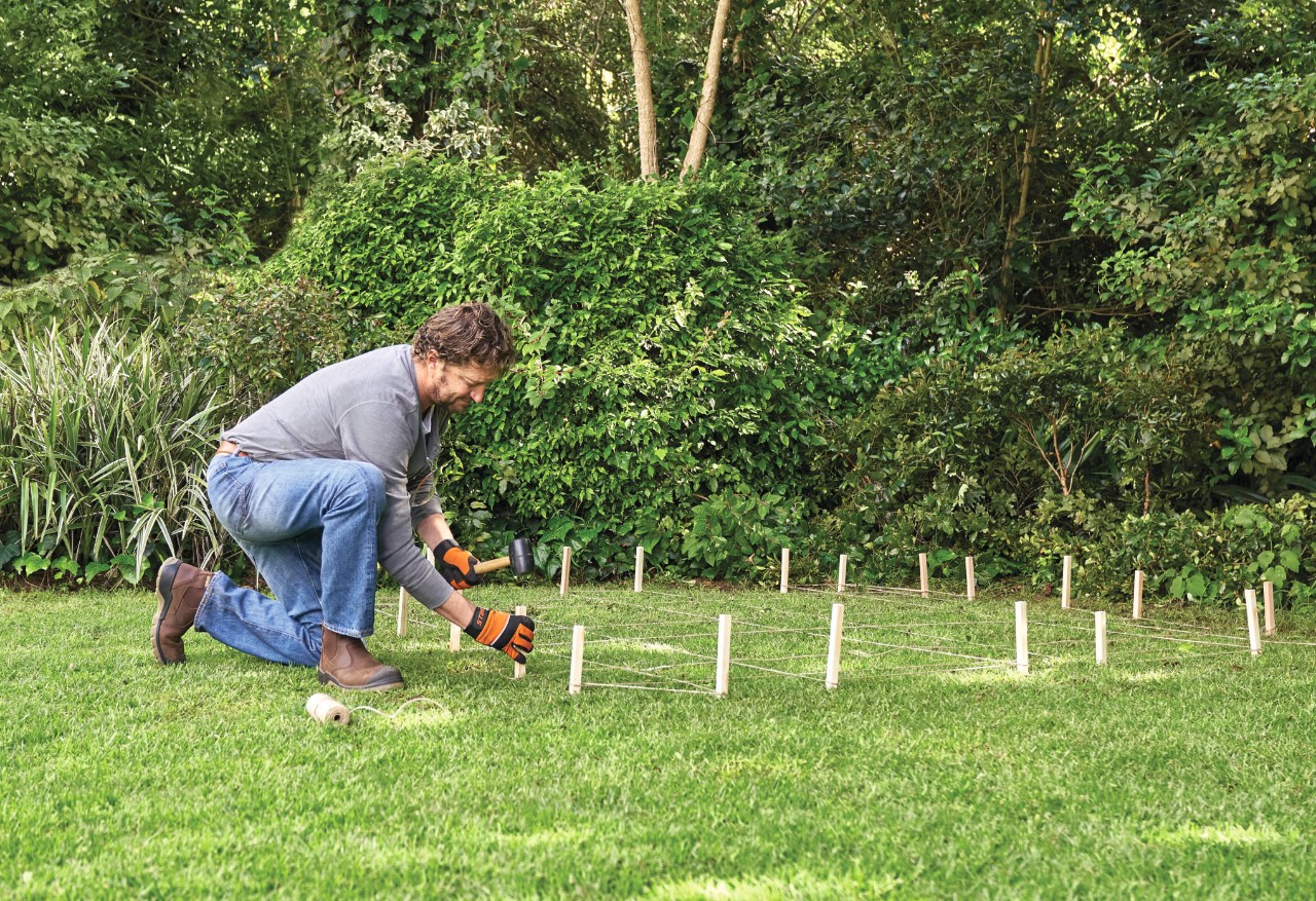 Comment construire un abri de jardin : homme délimitant les contours d’un abri de jardin sur la pelouse