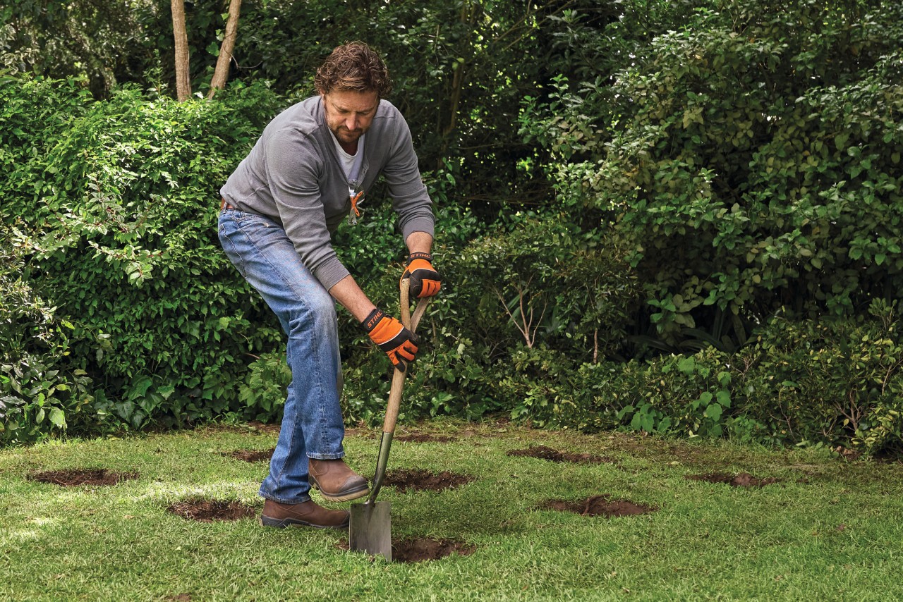 Hoe je een tuinhuis bouwt: een man die een schop gebruikt om 9 gaten te graven voor funderingen van palen