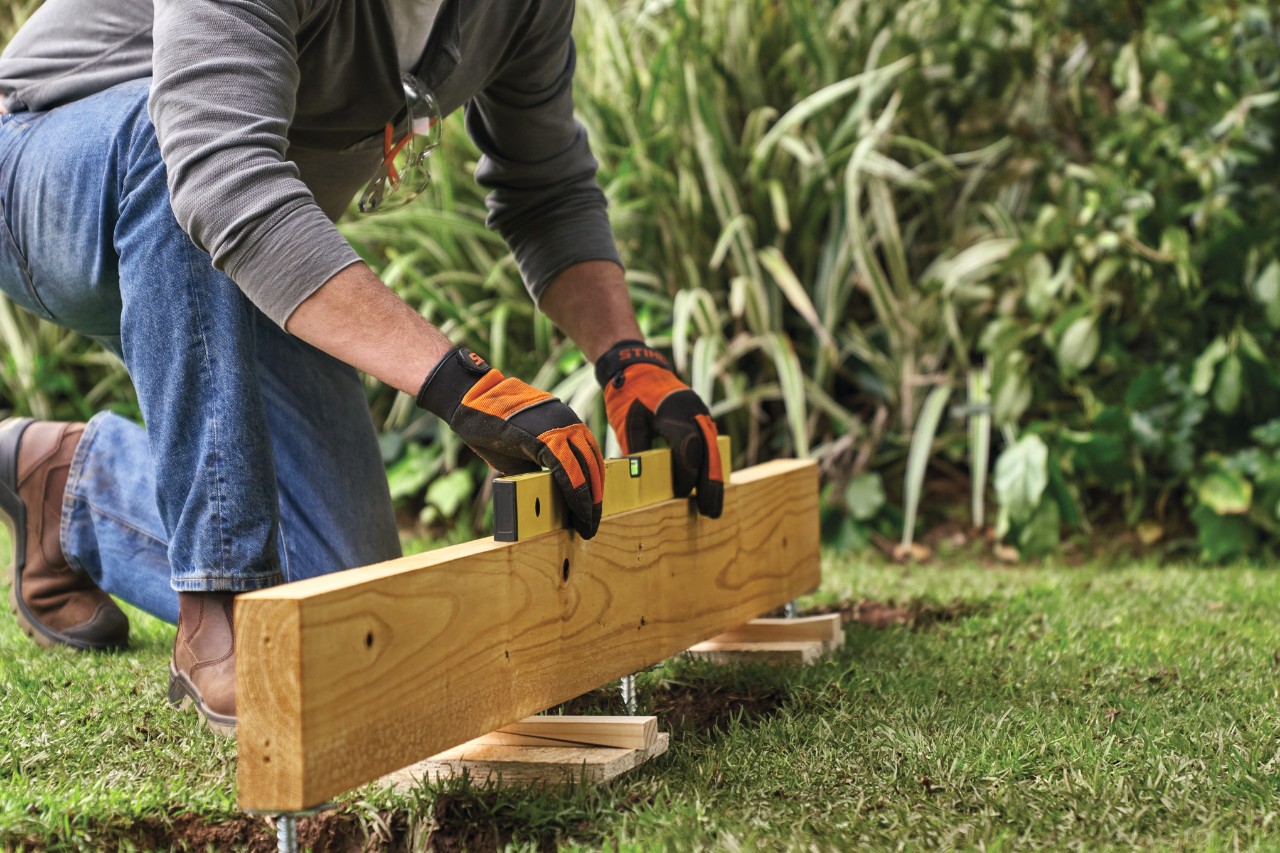 Comment construire une remise de jardin : personne vérifiant l’horizontalité de l’installation avec un niveau à bulle 