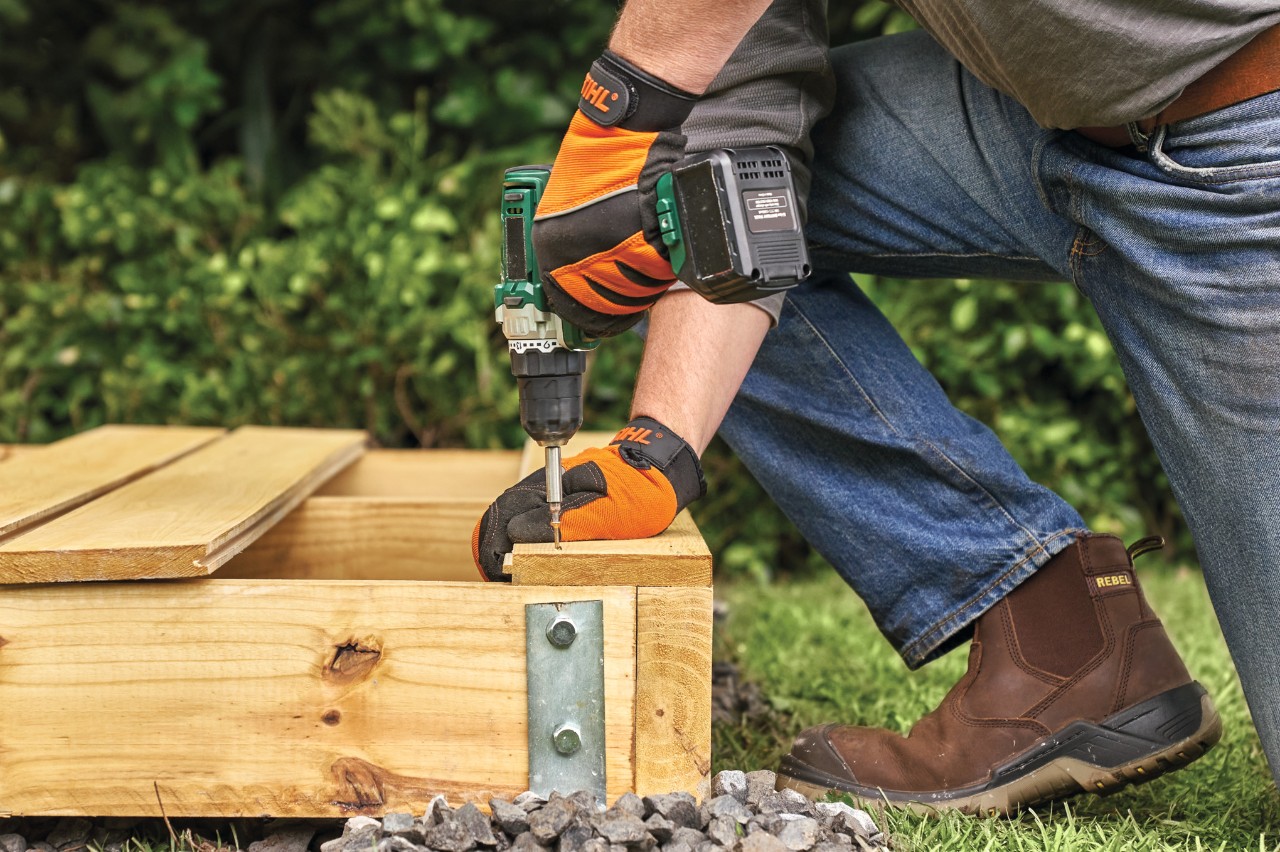 Comment construire un abri de jardin : planche à rainures et languettes vissée sur la base en bois de l’abri