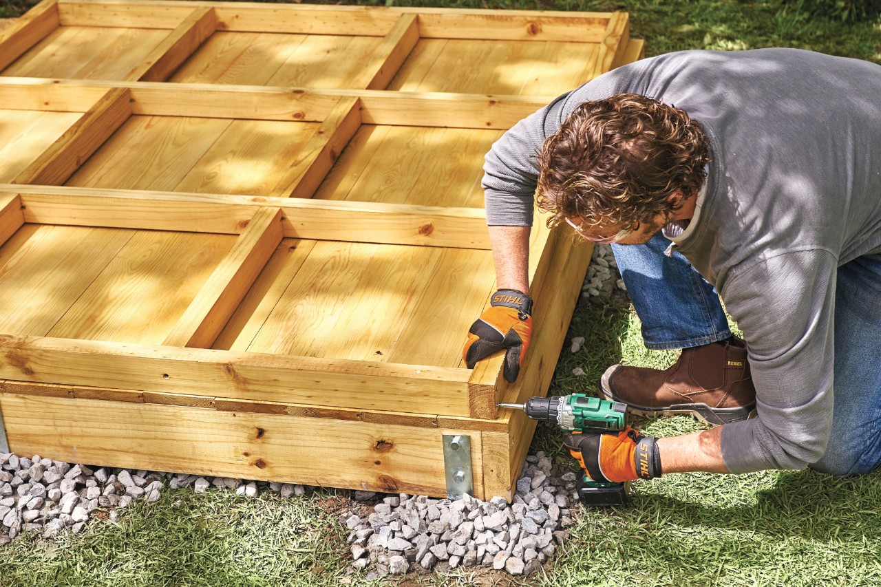 Comment construire un abri de jardin : homme en train de visser un panneau sur le châssis d’une paroi d’abri de jardin