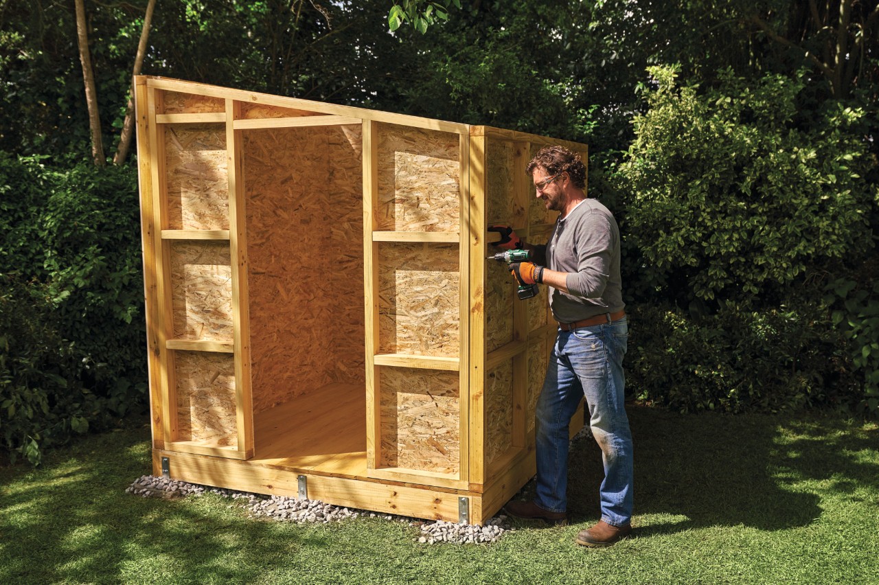 Comment construire un abri de jardin : homme vissant les parois assemblées d’un abri de jardin