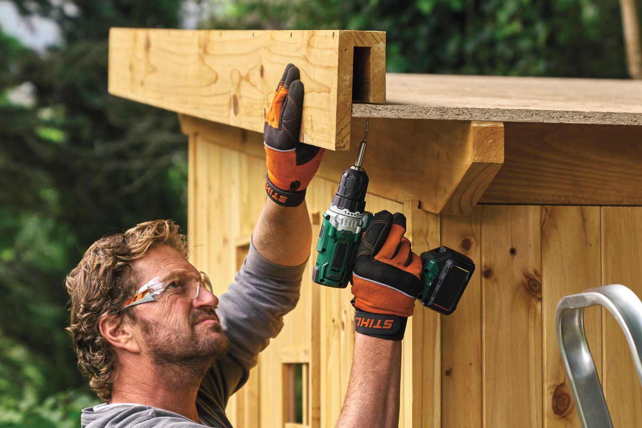 Comment construire un abri de jardin : homme montant un bord de toit pré-assemblé sur le toit d’un abri de jardin