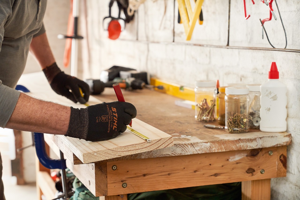Un homme portant des gants de protection STIHL marque des trous de forage sur une planche de bois