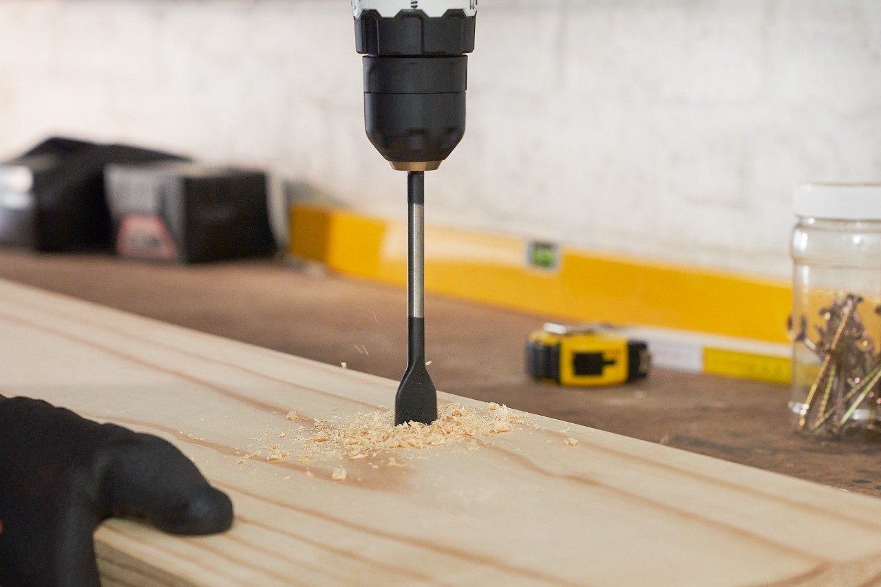 Une personne perce des trous dans une planche de bois pour construire un support de rangement pour outils de jardin