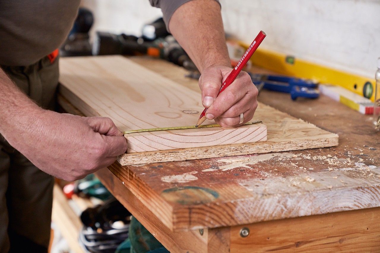 Homme marque des trous de forage sur une planche de bois pour fabriquer un support de rangement à outils de jardin