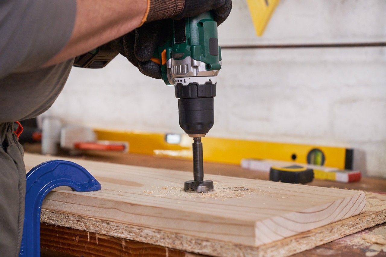 Homme utilise une perceuse plate pour percer des trous dans une planche pour un support pour outils de jardin