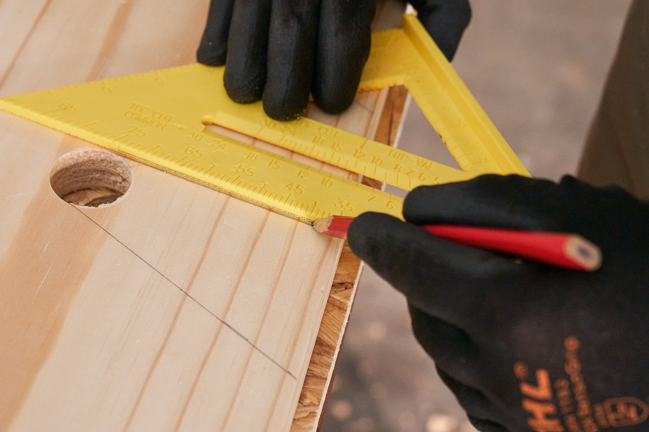 Quelqu’un trace des lignes sur une planche de bois avec un crayon et une équerre pour marquer les évidements 