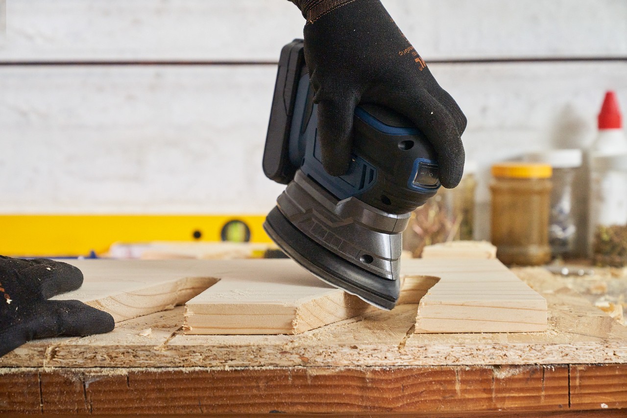 Main en train de poncer une planche avec une meuleuse sur le support de rangement pour outils de jardin