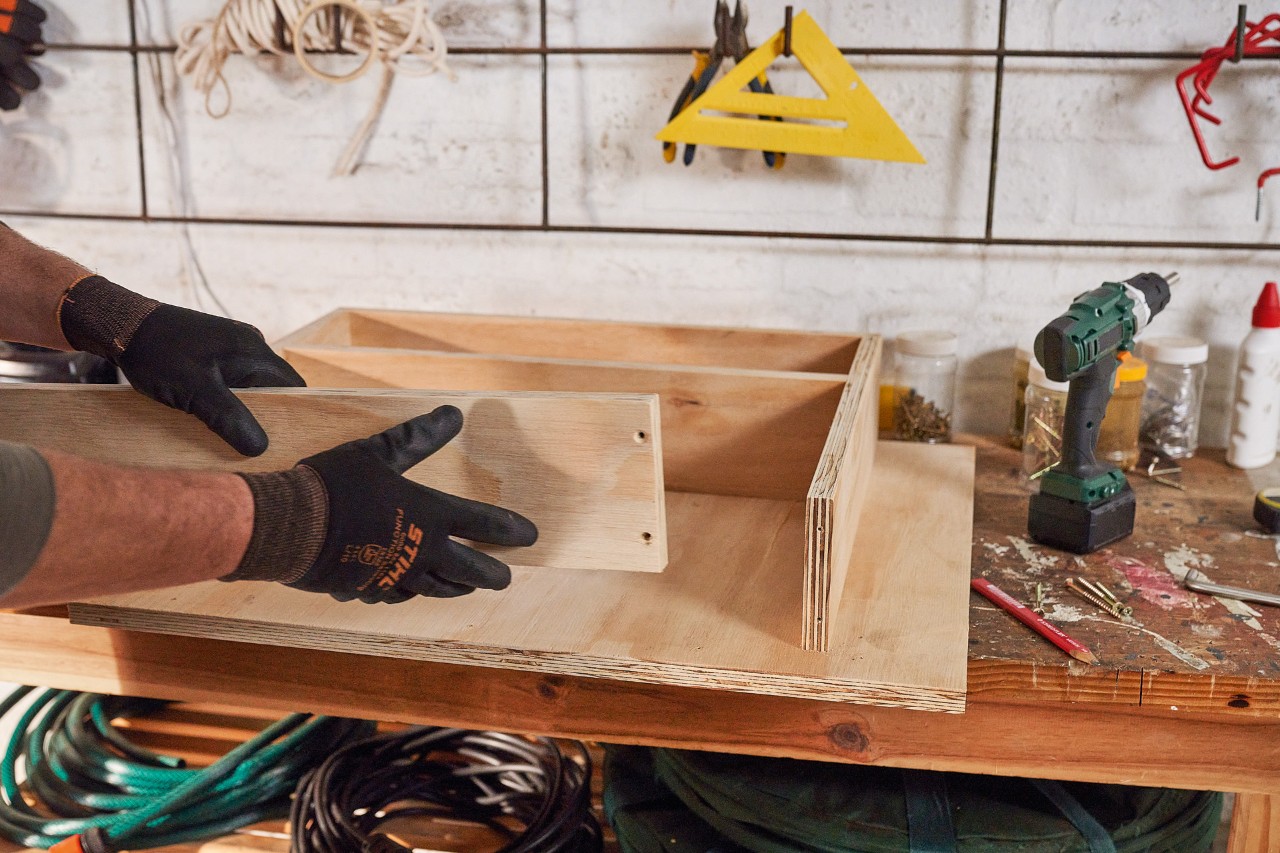 Un homme fabrique des tiroirs à partir de planches de bois pour son rangement pour tondeuse à gazon 