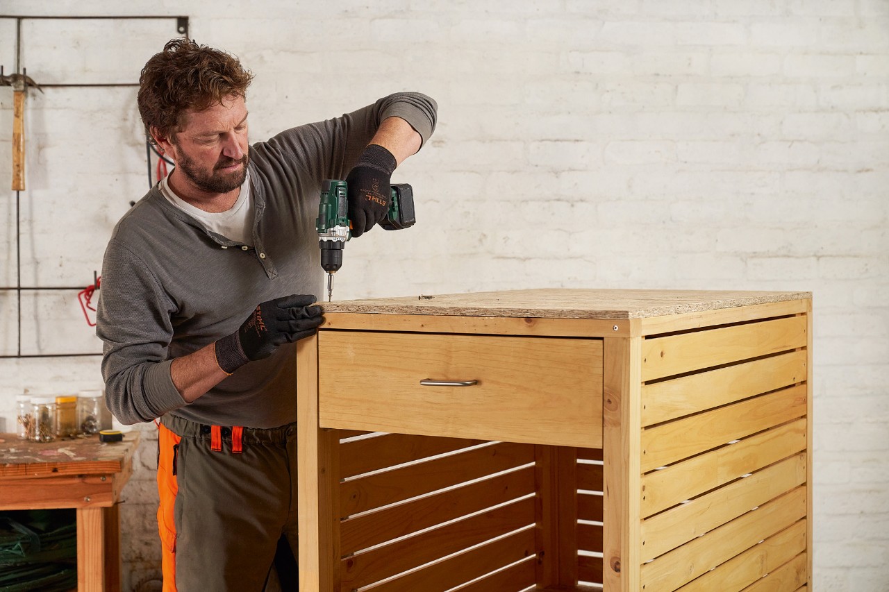 Un homme visse une planche d’OSB sur le rangement pour tondeuse à gazon en guise de toit