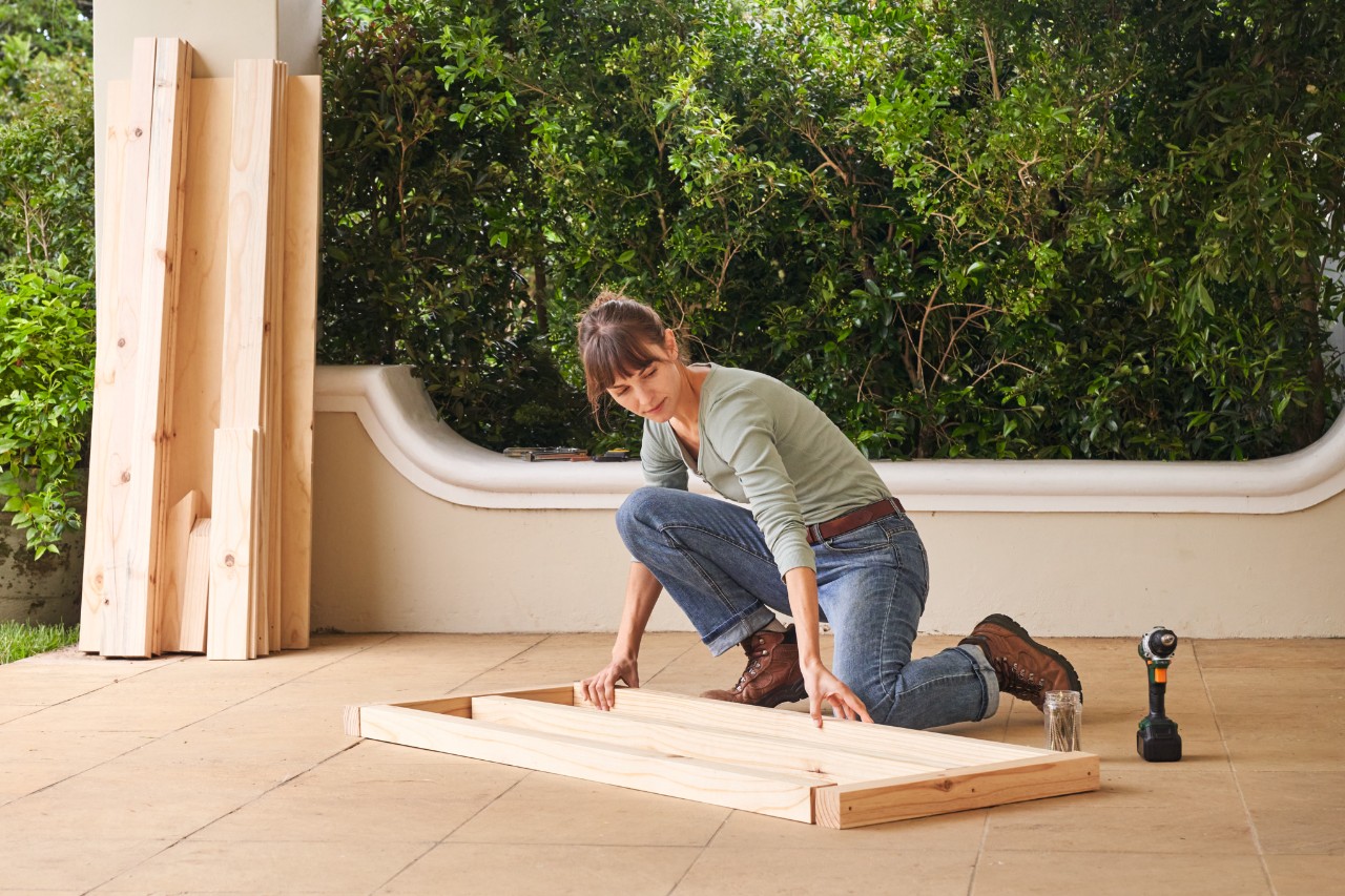 Femme disposant les pièces en bois pour la structure inférieure du toit de la serre à tomates sur une terrasse