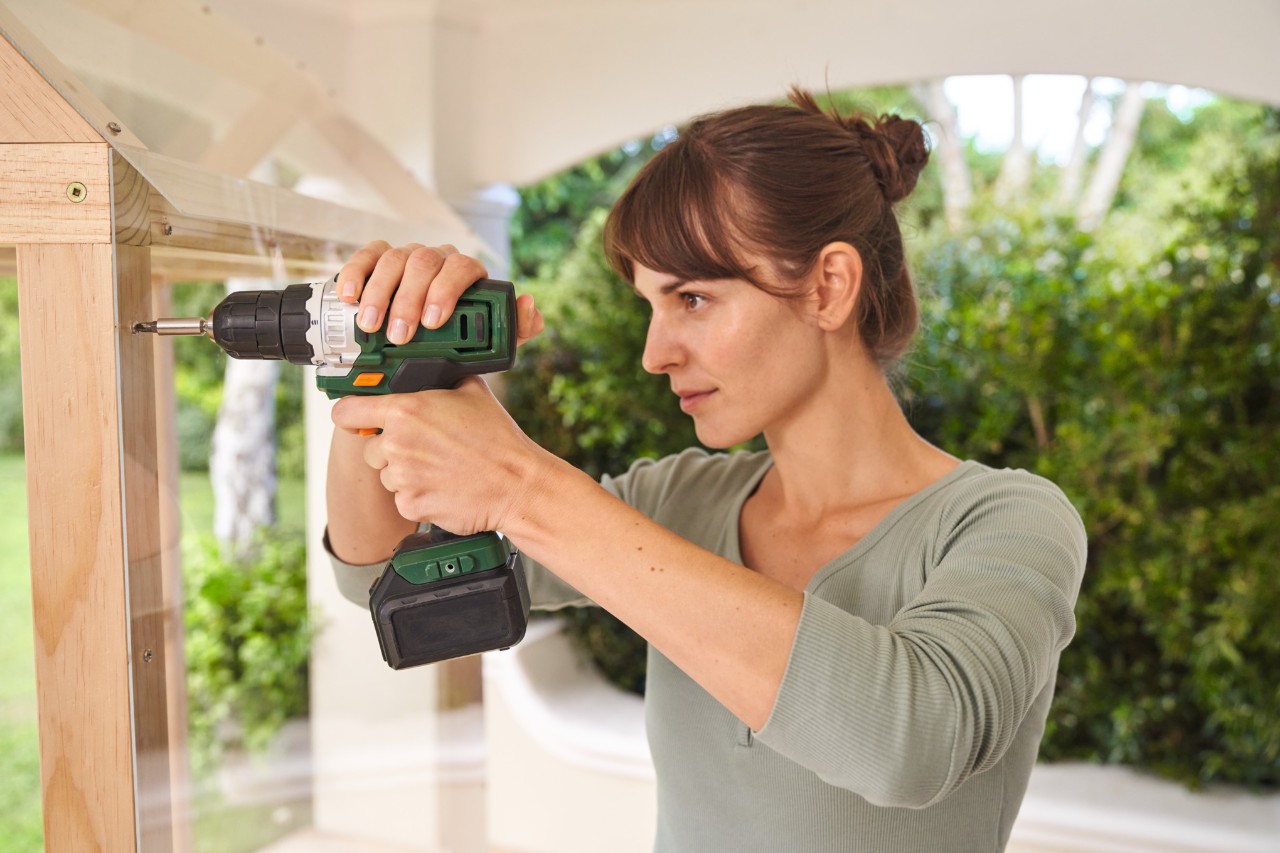 Une femme visse des plaques de plexiglas sur son abri à tomates