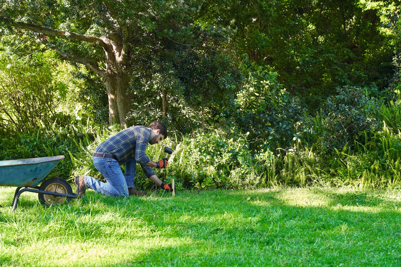 Un homme délimite la surface destinée à accueillir une prairie de fleurs sauvages avec une corde à linge et de piquets