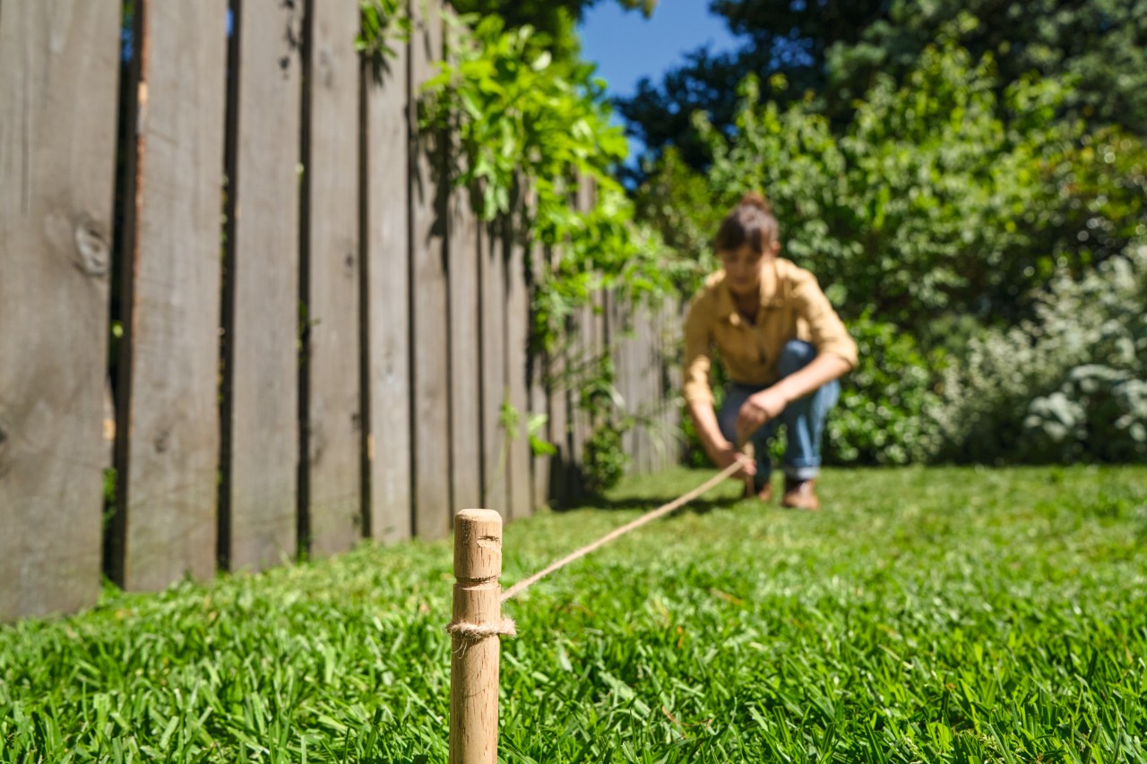 Une femme repère le bord prévu pour la bande fleurie avec des piquets en bois et une ficelle