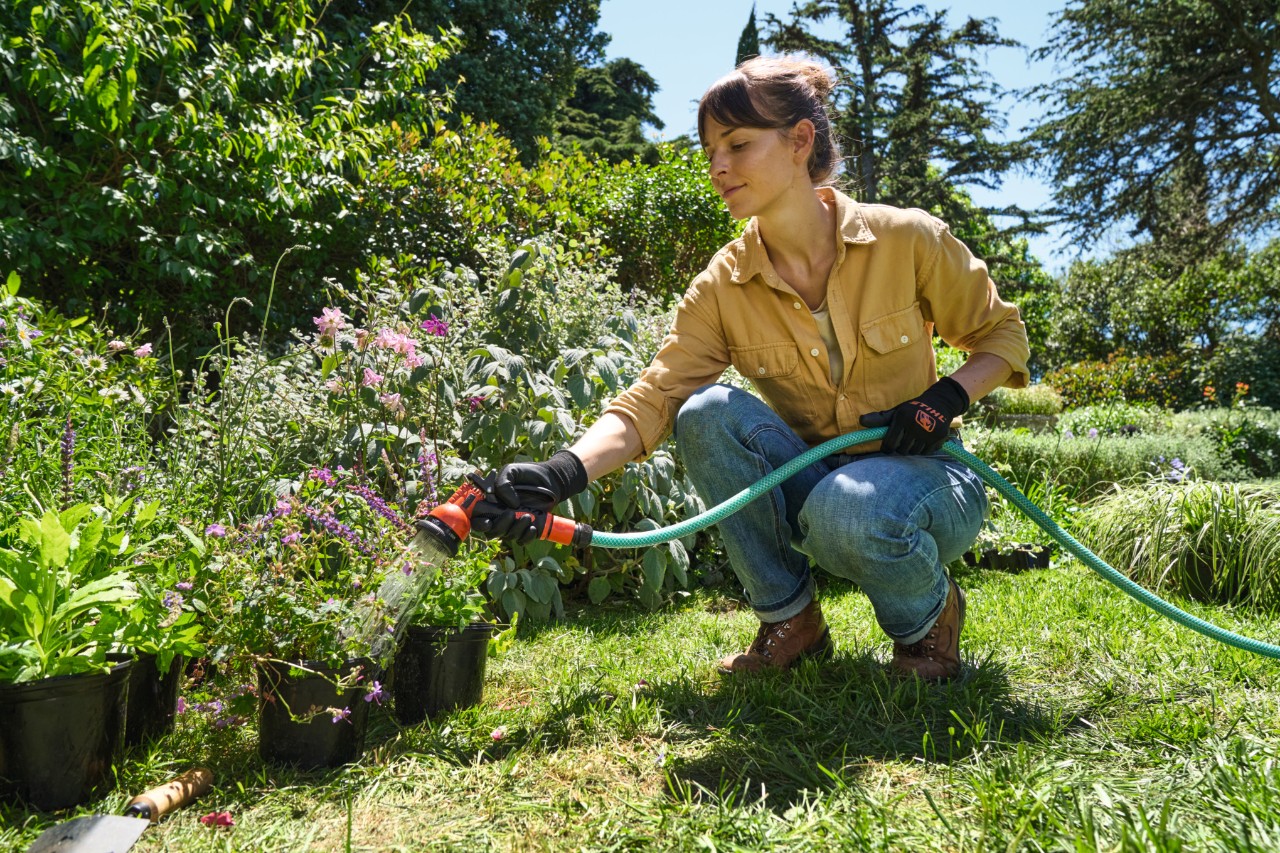 Une femme sur une pelouse arrosant des plantes en pot avec un tuyau d’arrosage
