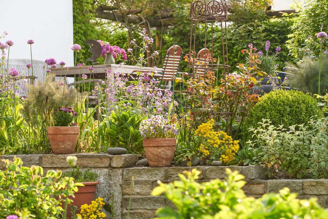 Jardin suspendu printanier avec mur et pots de fleurs, table de jardin avec chaises en arrière-plan 
