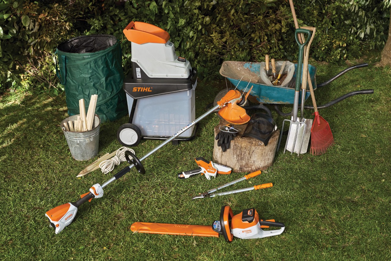 Un taille-haie, un broyeur de jardin, une brouette et d’autres outils et équipements disposés sur une pelouse