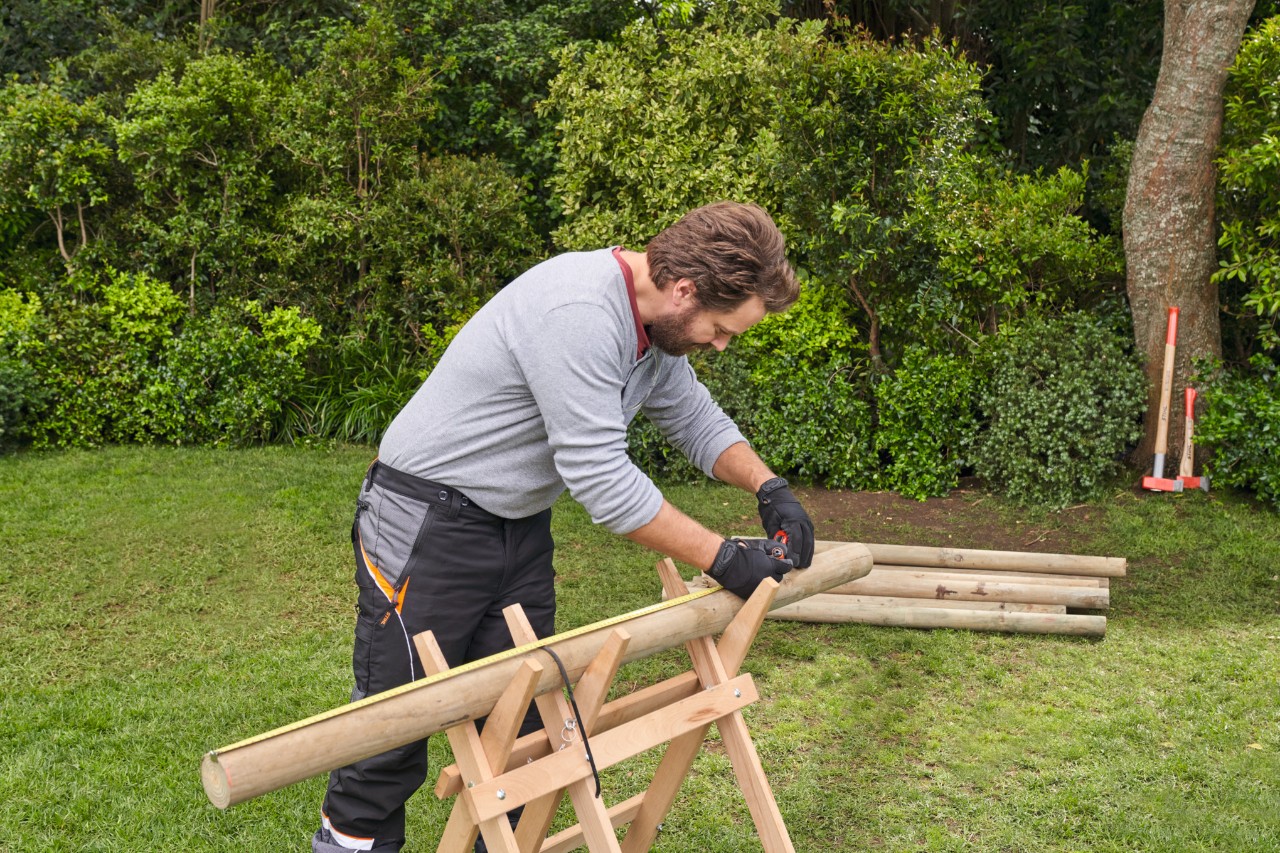 Homme mesurant des branches sur un chevalet en bois et marquant les longueurs