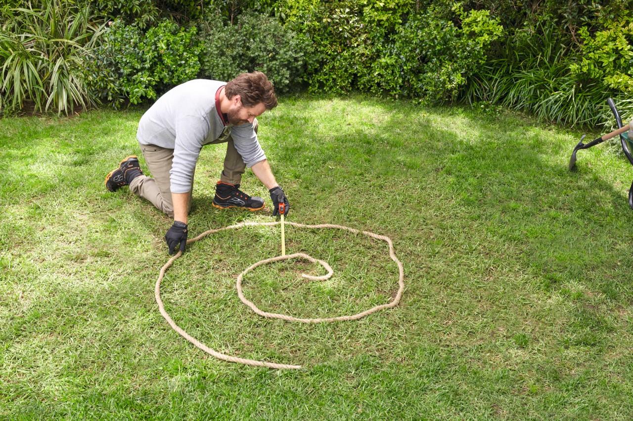 Homme sur une pelouse marquant le tracé prévu de la spirale aromatique avec une corde