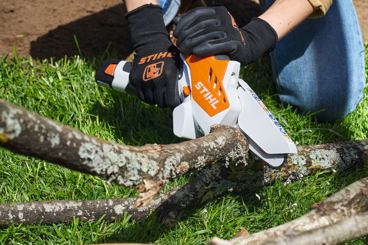 Personne portant des gants de protection sciant des morceaux de branches avec une scie de jardin à batterie STIHL GTA 26